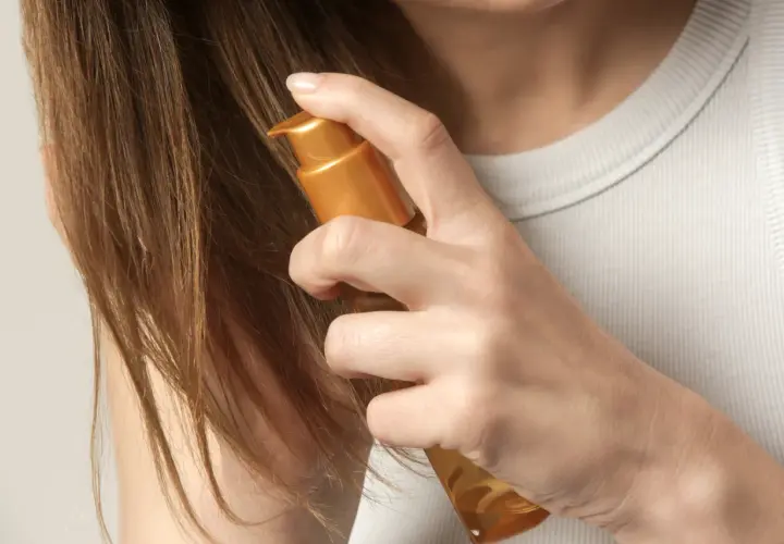 Delikatne olejowanie włosów rozjaśnianych złotym serum. Dłoń aplikuje produkt na brązowe pasma, przywracając im blask i nawilżenie.