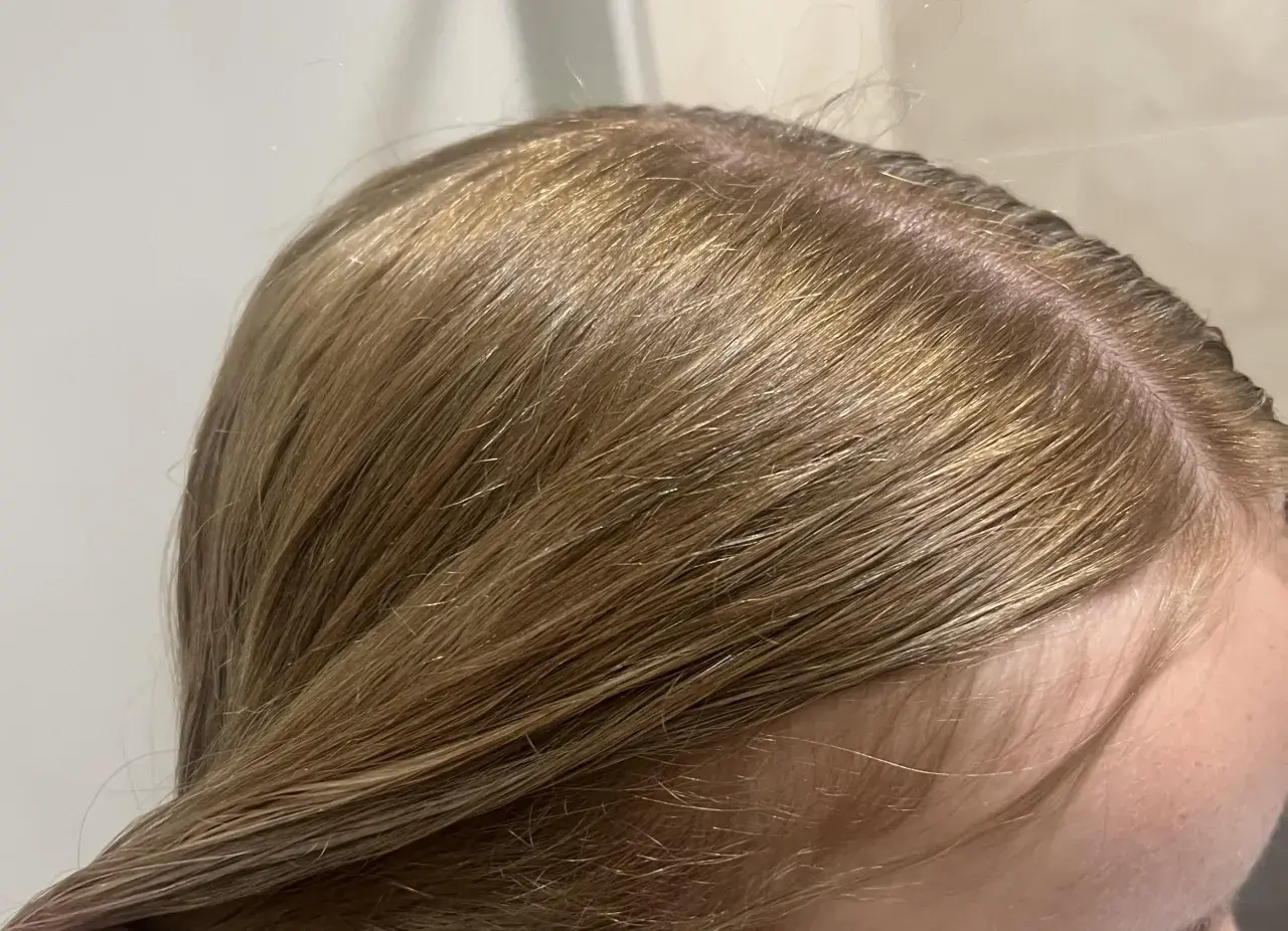 Zbliżenie na blond włosy z widocznymi pomarańczowymi tonami przy skórze głowy.