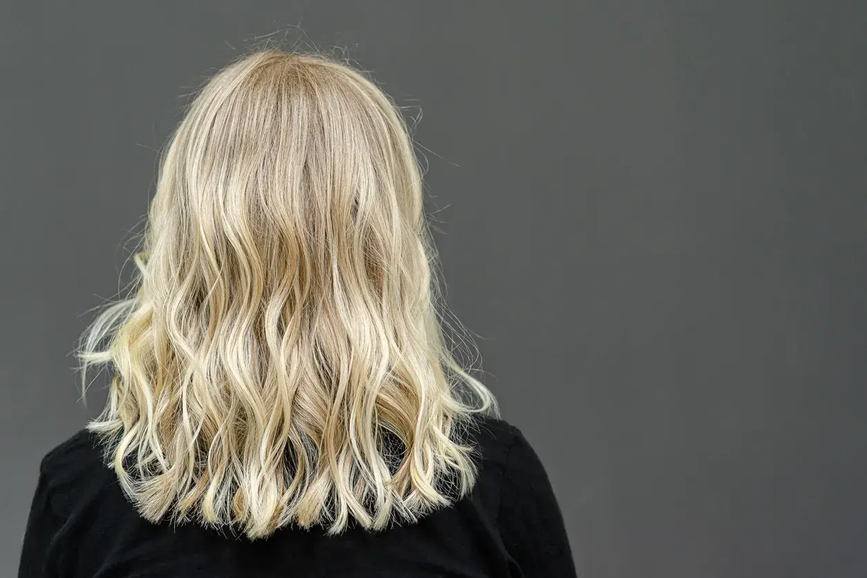 Widok z tyłu na falowane, blond włosy kobiety na ciemnym tle.