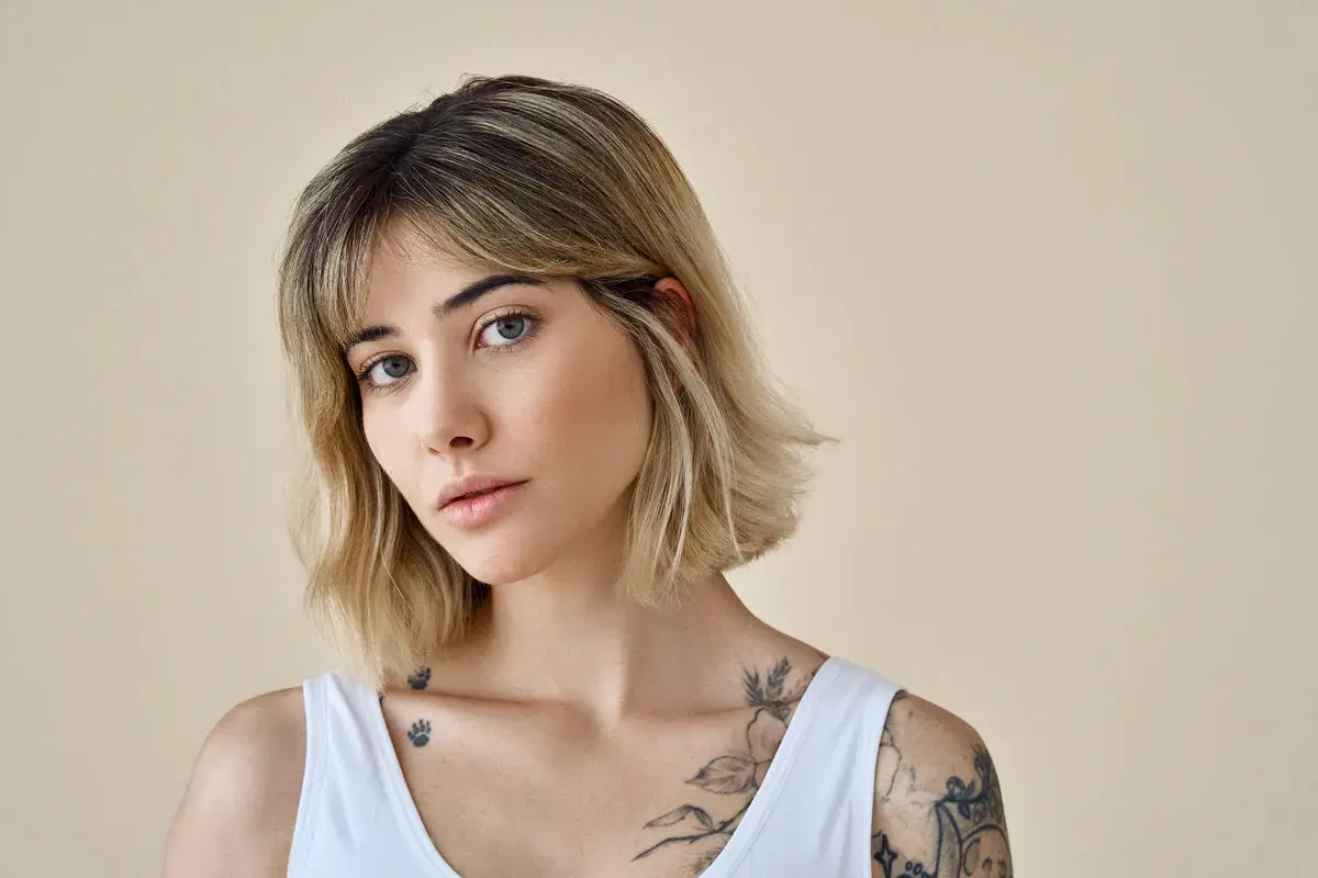 Kobieta z tatuażami i modną, postrzępioną fryzurą typu choppy bob.