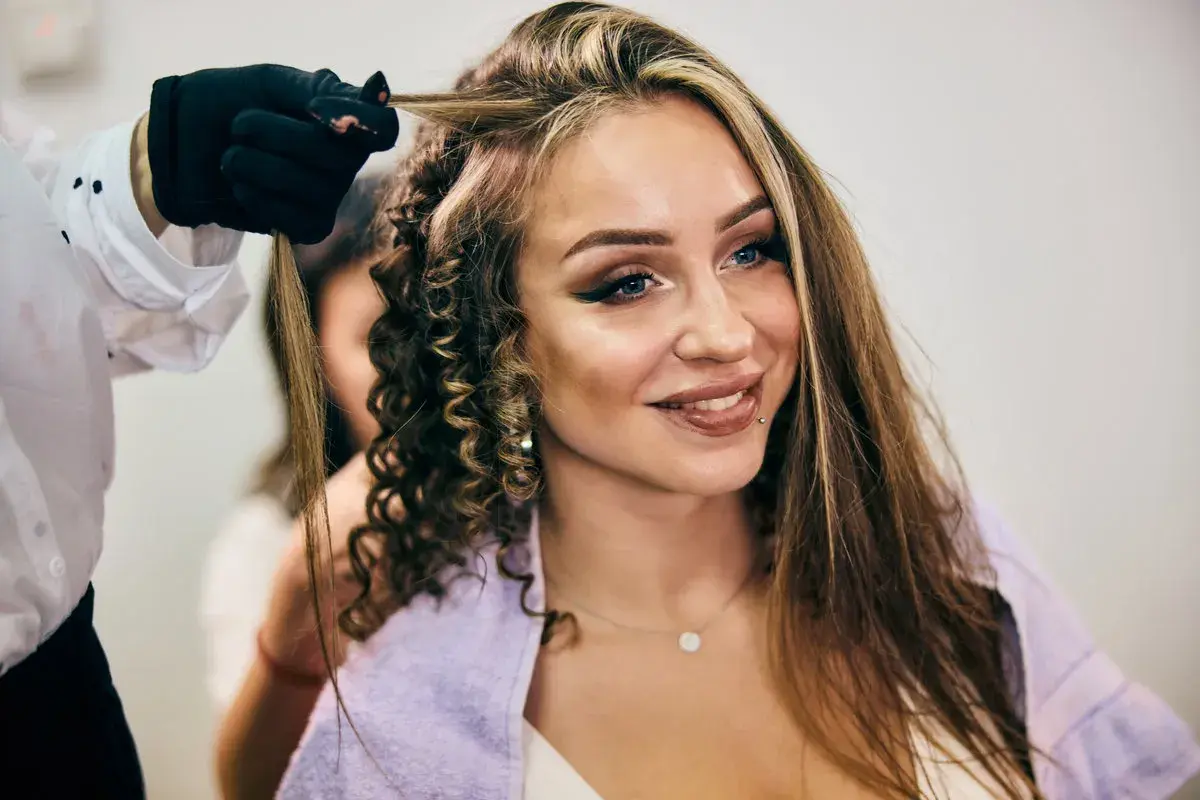 Stylist tworzy loki na włosach kobiety z widocznymi chunky highlights.