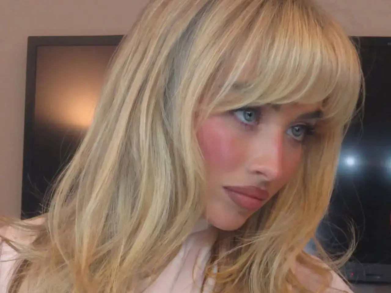 Blondynka z niebieskimi oczami i modną grzywką francuską, lekko zarumieniona.